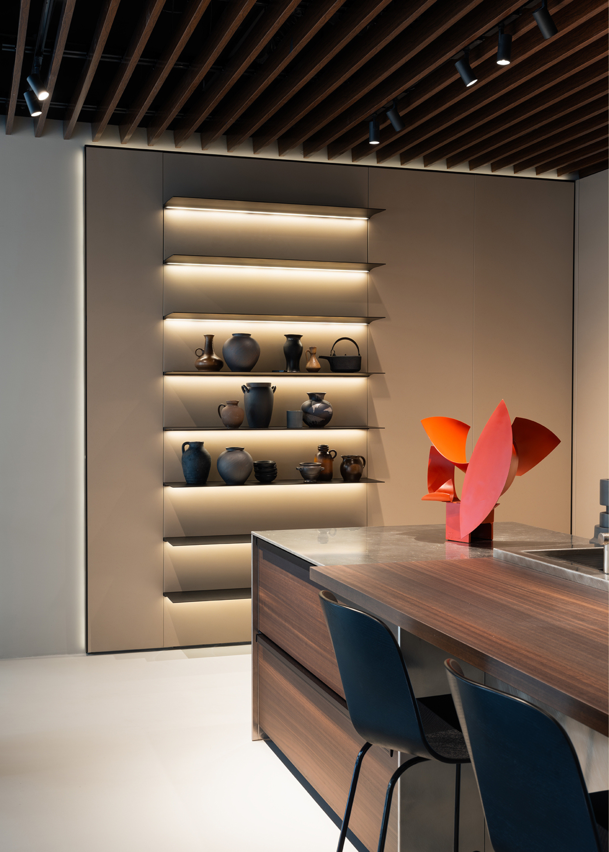 A kitchen a backlit shelving system beside an island