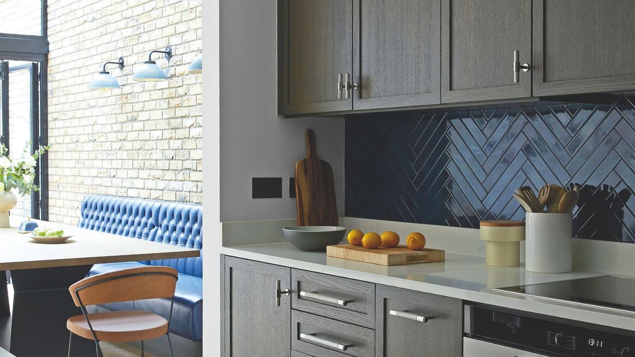 A small kitchen with gray cabinets and a blue chevron tile backsplash