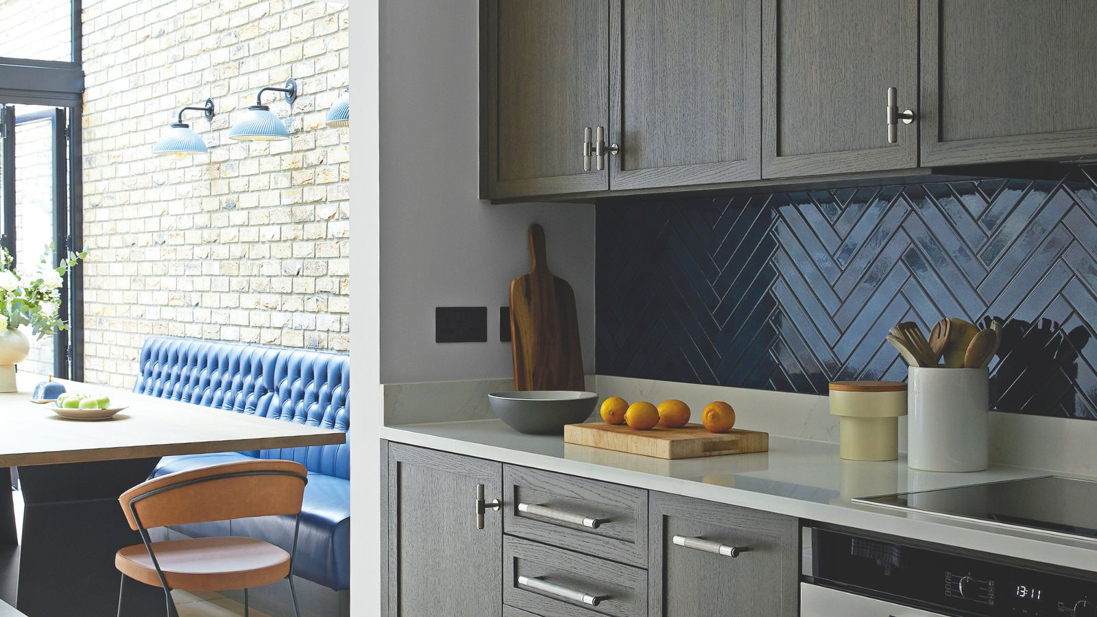 A small kitchen with gray cabinets and a blue chevron tile backsplash