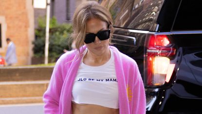 Jennifer Lopez wearing a slogan crop top with a pink cardigan slouchy jeans and a dior wicker bag
