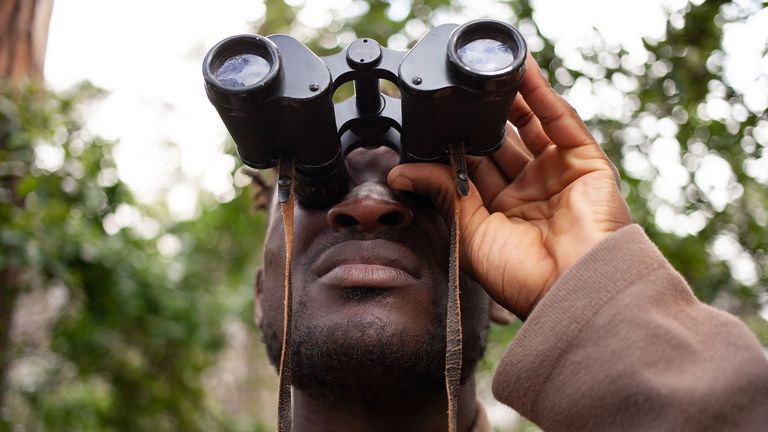 best binoculars for birdwatching: Close up of man looking upwards through a pair of binoculars