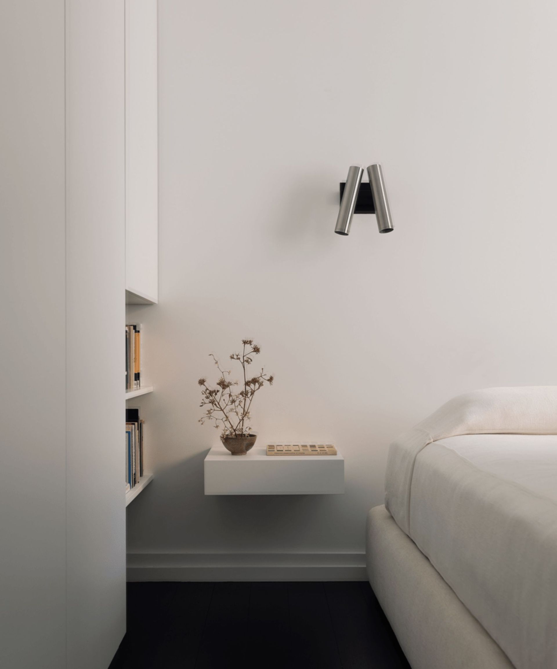 Minimalist bedroom with white walls, floating bedside table, silver sconce and built-in bookshelf
