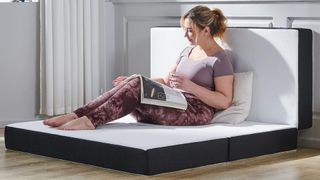 A blonde woman uses a trifold mattress as a sofa