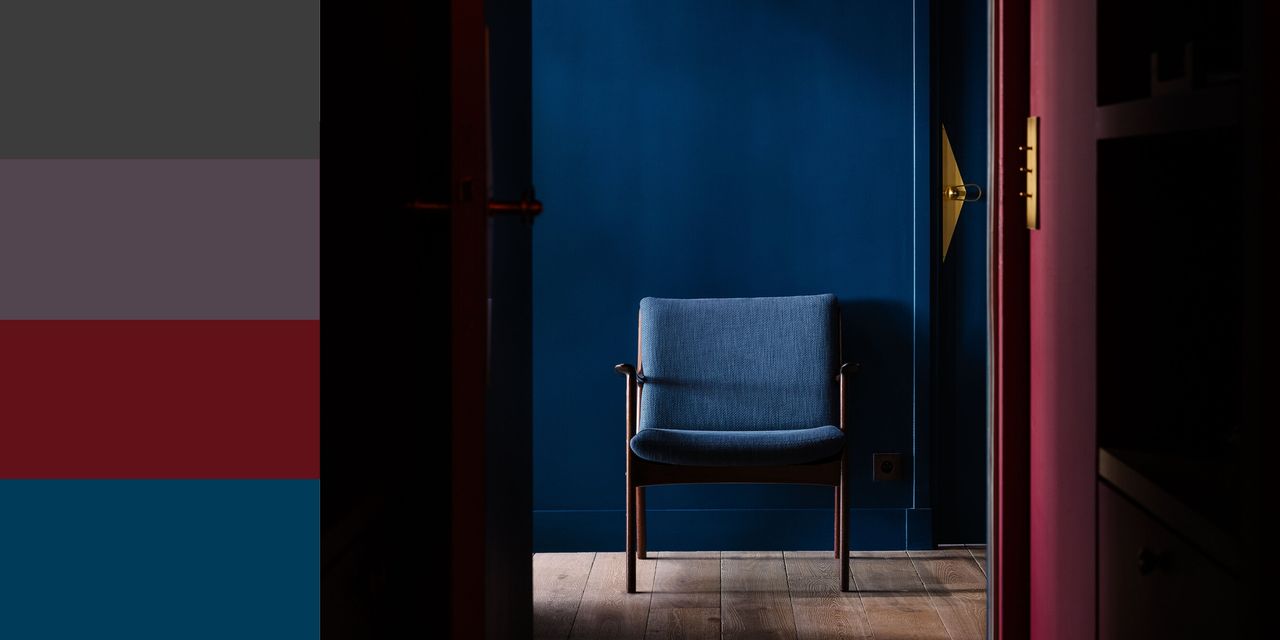 Image of a hallway that is painted in a deep red color with a deep blue wall at the end of the hall. There is a blue accent chair at the end of the hall as well. Three gold pendant lights line the hallway. There are four paint samples of charcoal, plum, red, and mid-toned blue on the left side.