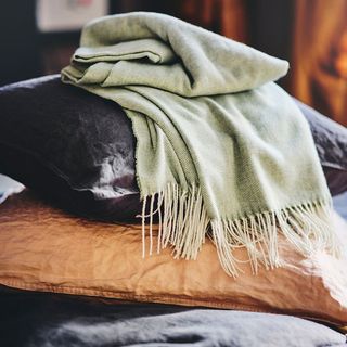 A green throw blanket with fringed bottoms laying on top of two leather throw pillows