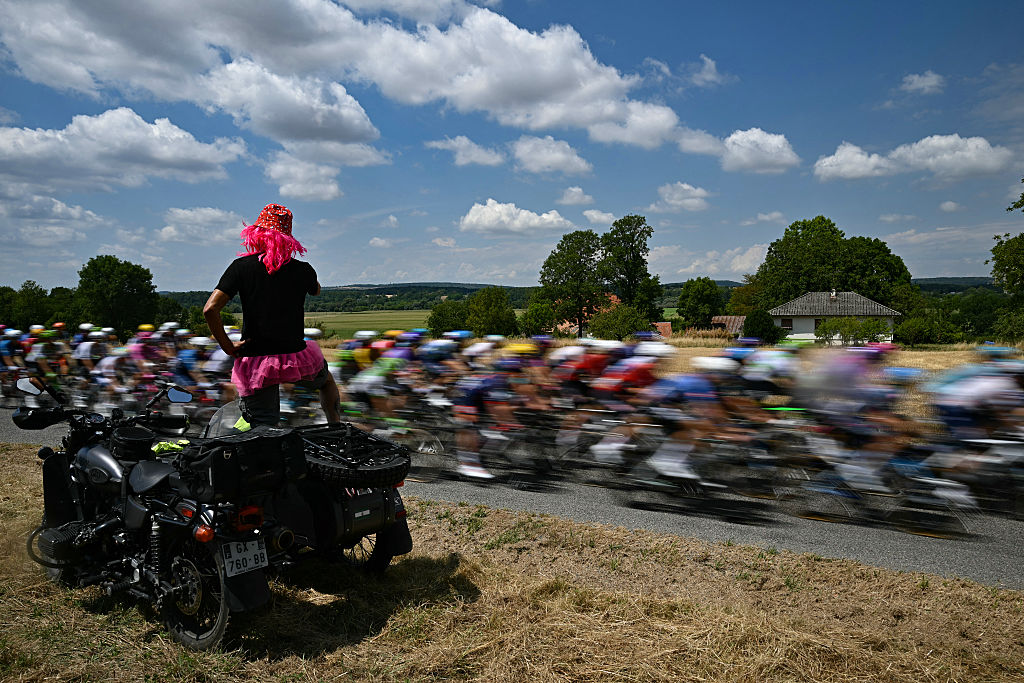A spectator atop a motorcycle watches the pack of riders (peloton) cycle past during the 13th stage of the 113th edition of the Tour de France cycling race, 205,8 km between Dole and Belfort in eastern France, on July 17, 2026. (Photo by Loic VENANCE / AFP)