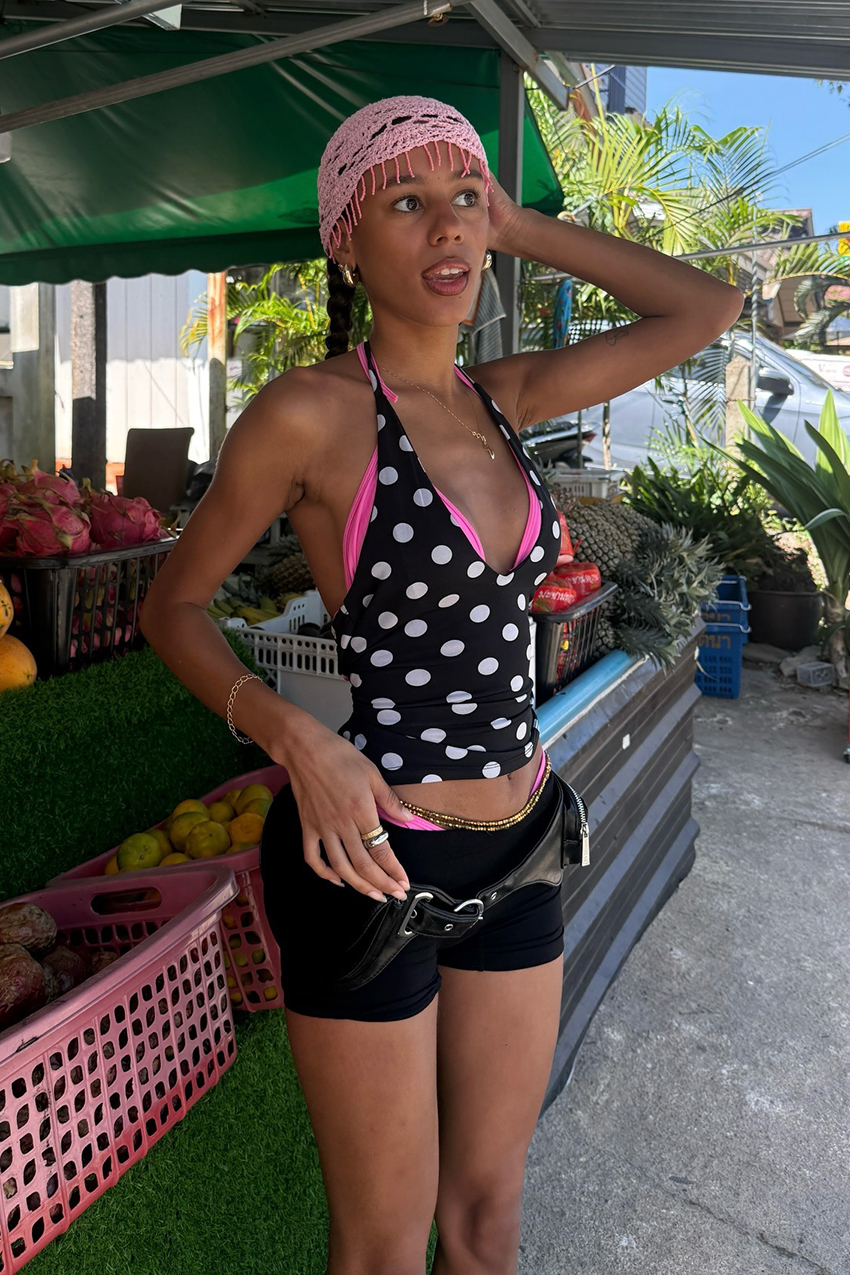 a woman wearing a pink crochet cap, polka dot tank top, and black shorts