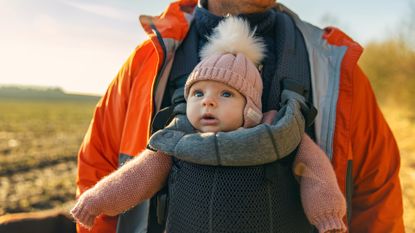 A baby girl is shown being carried by her father in a baby carrier while out on a walk in the countryside. 