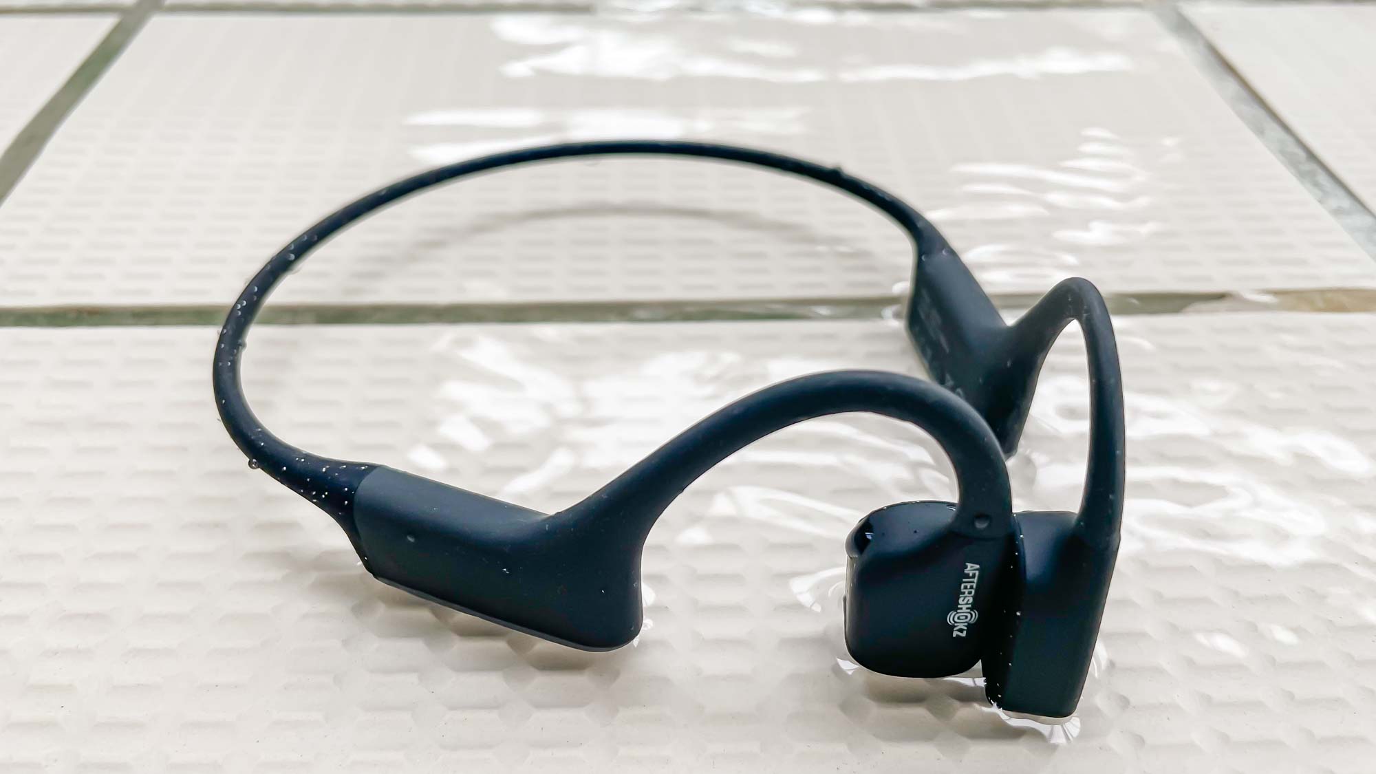 Shokz OpenSwim in a puddle of water next to a pool