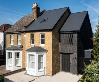 dark brick side extension on front of property that has a slate roof but lighter brick facade