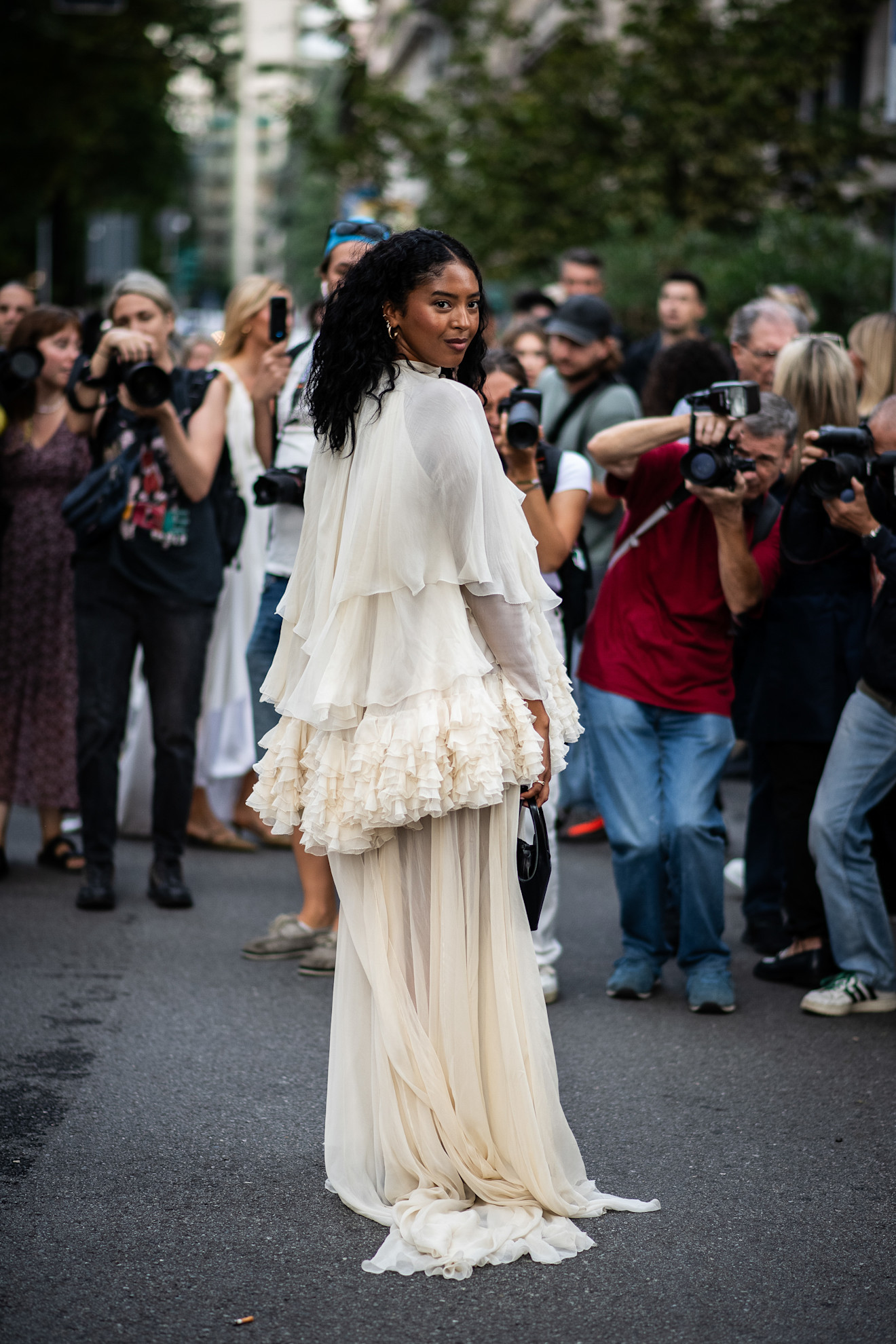 a woman in a white ruffled dress standing on the street in front of a crowd of photographers