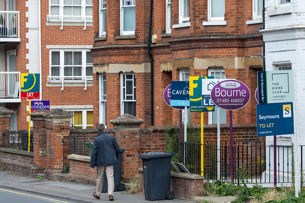Man walking down street with 'for sale' signs
