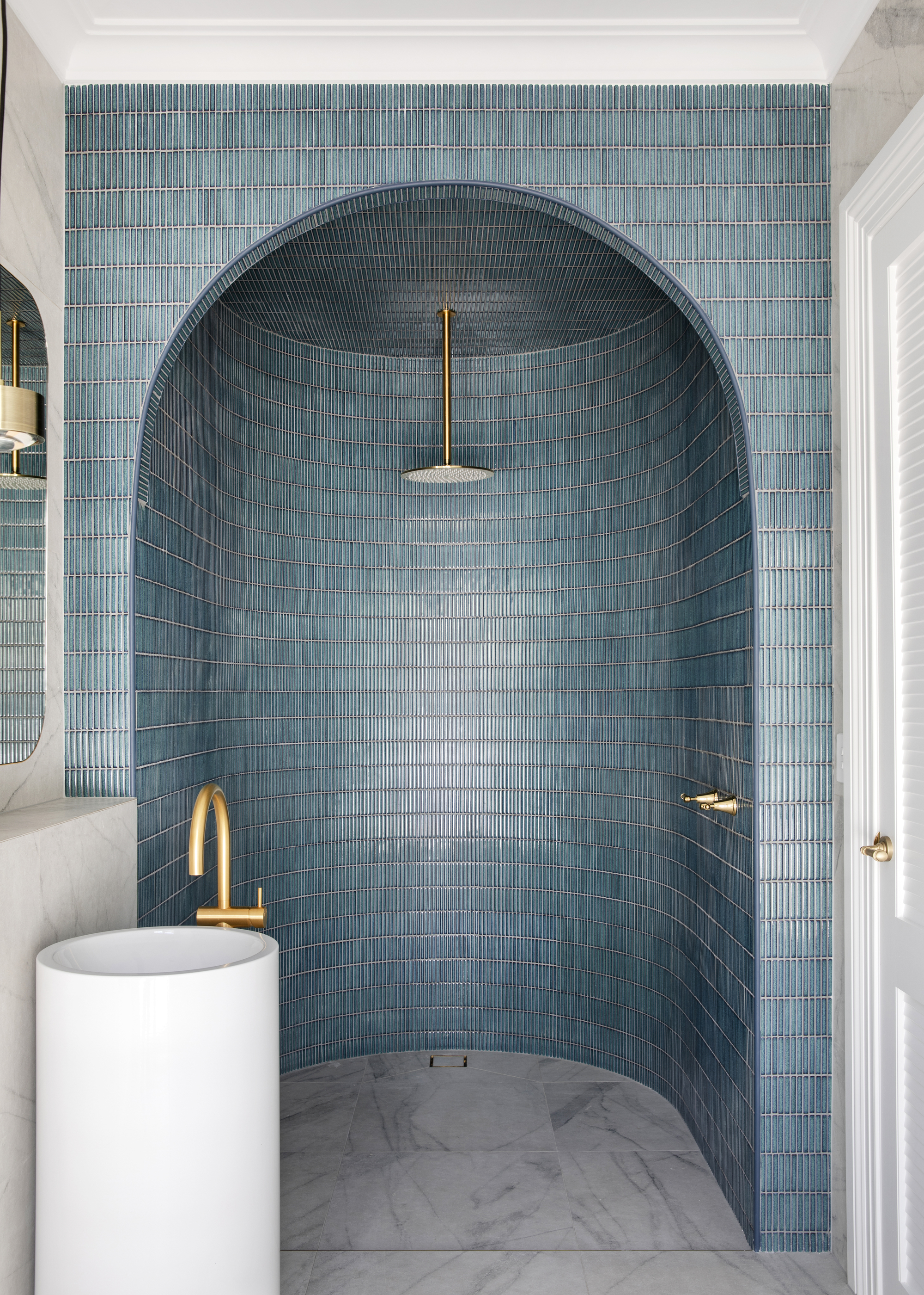 A curved wall-in shower enclosure with blue zellige tiles and marble stone flooring