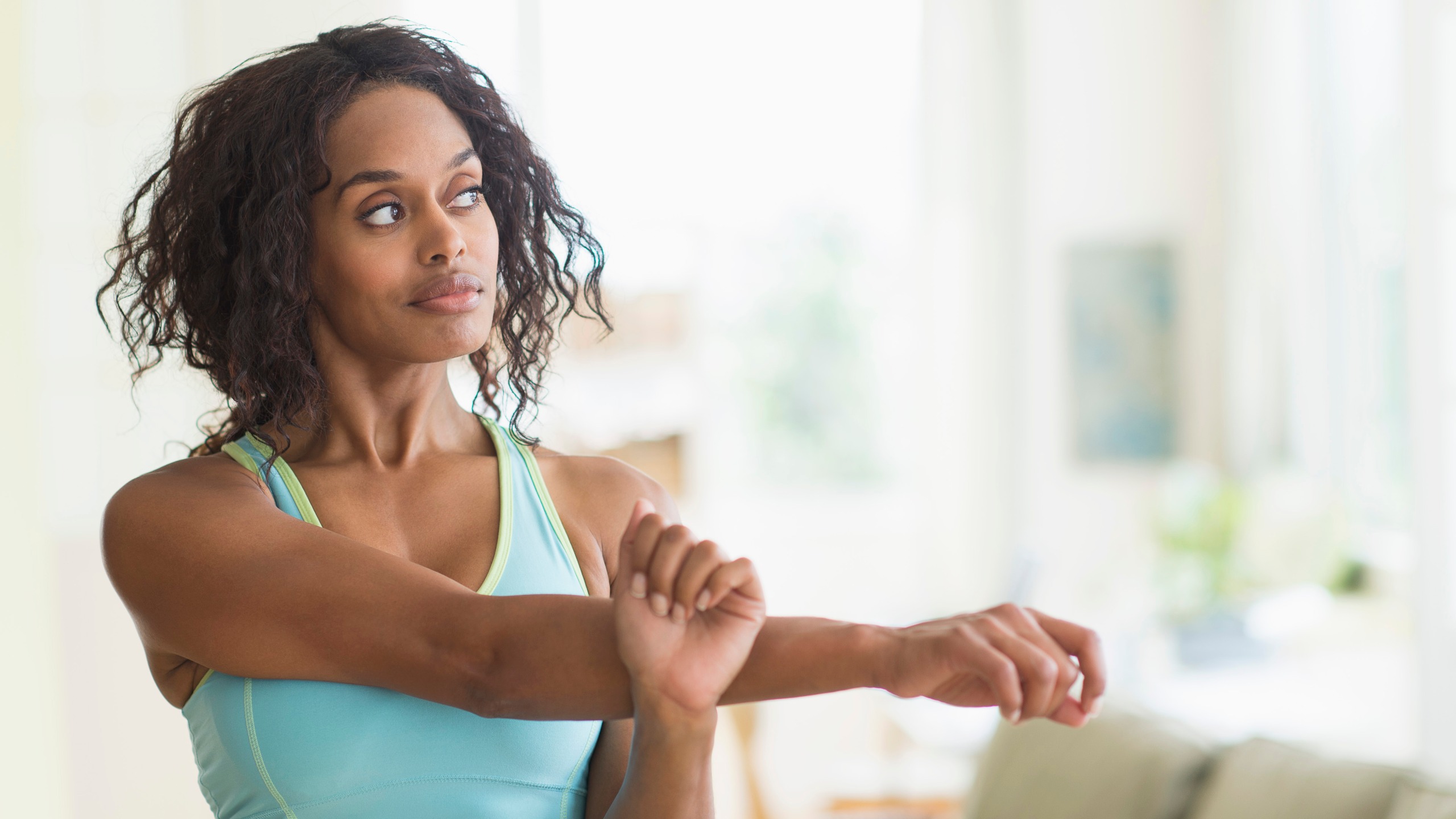 A woman in a sports top stretches her right arm across her chest and pulls it closer with her left hand. 