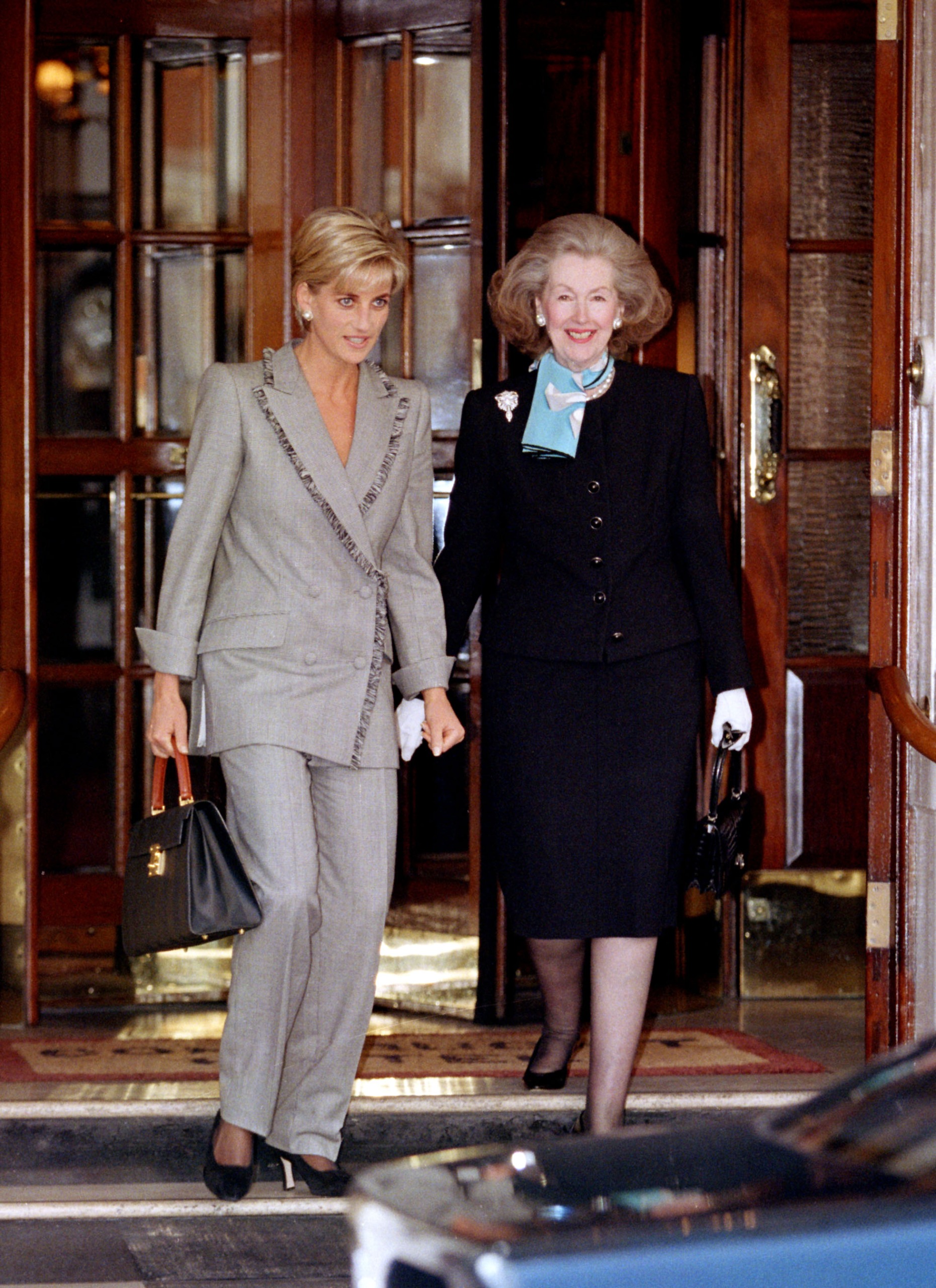 Princess Diana walking out of a hotel with Raine Spencer wearing a gray suit