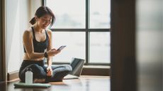 Woman looking down at phone smiling with water bottle and laptop