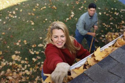 A couple cleaning the gutters of their home