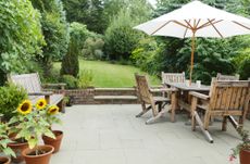 A grey patio with wooden garden table and chairs.