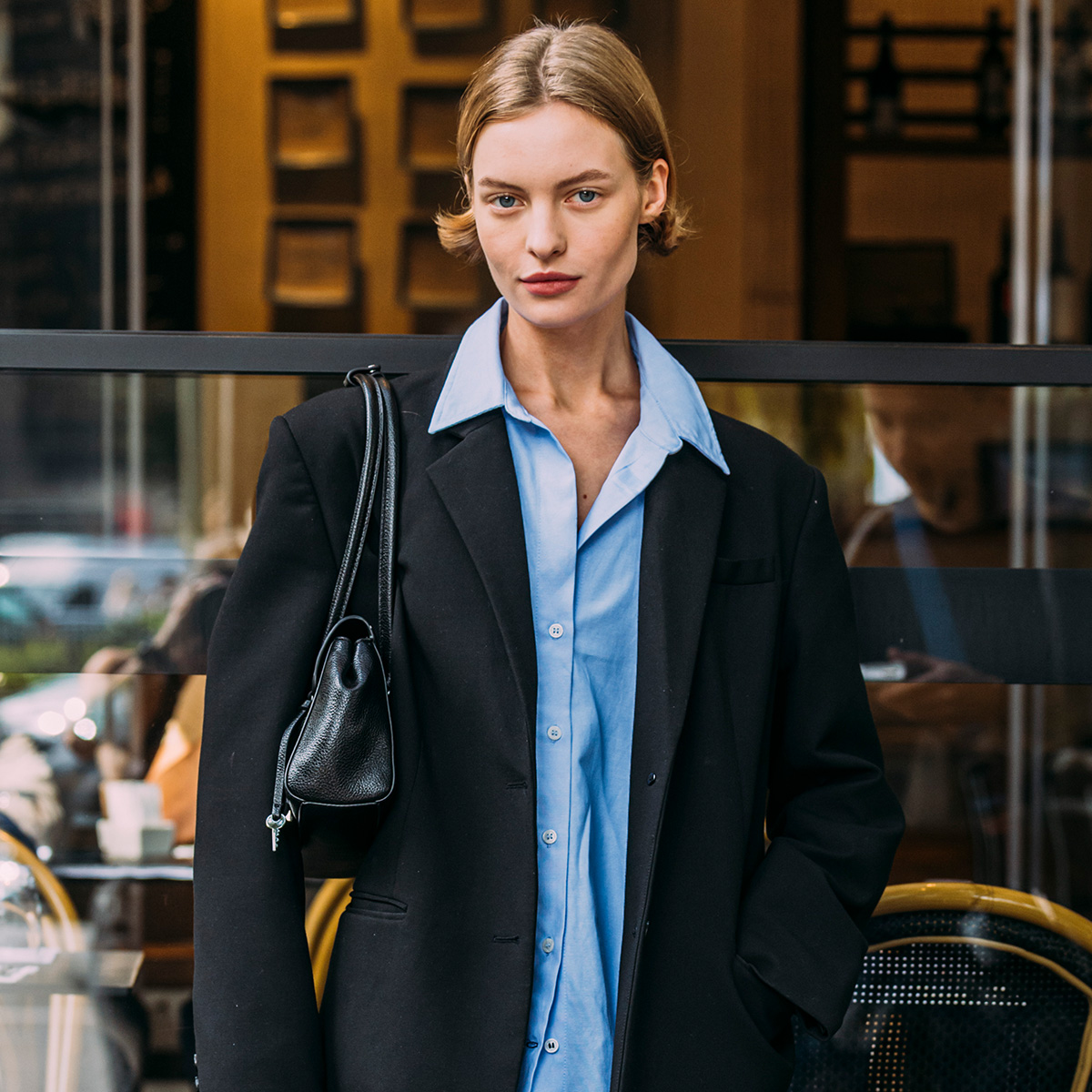 A woman wears a blue button-up, black blazer, and black handbag.