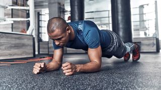 Man holds forearm plank position in gym