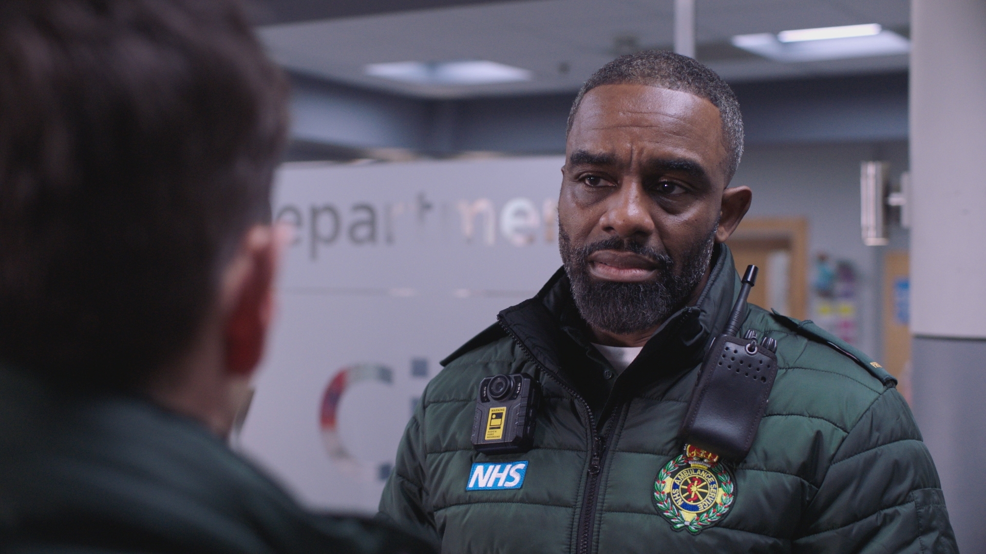 Jacob Masters looking tired and talking to Iain Dean in Holby ED.