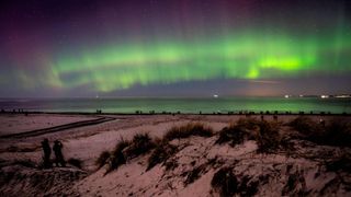 green auroras in the sky above a snowy riverbank
