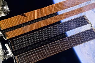 Dwarfed by the two legacy solar arrays, NASA astronaut Shane Kimbrough and Thomas Pesquet of ESA work to secure the first of six ISS Roll-Out Solar Arrays (iROSA) on the port (left) side of the International Space Station on June 16, 2021.