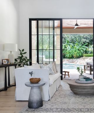 A living room with a white sofa and floor-to-ceiling glass doors opening up to a pool