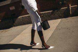 A street style shot from New York Fashion Week of a guest wearing white slingback heels, white capris, white blazer, and a black bucket basket bag.