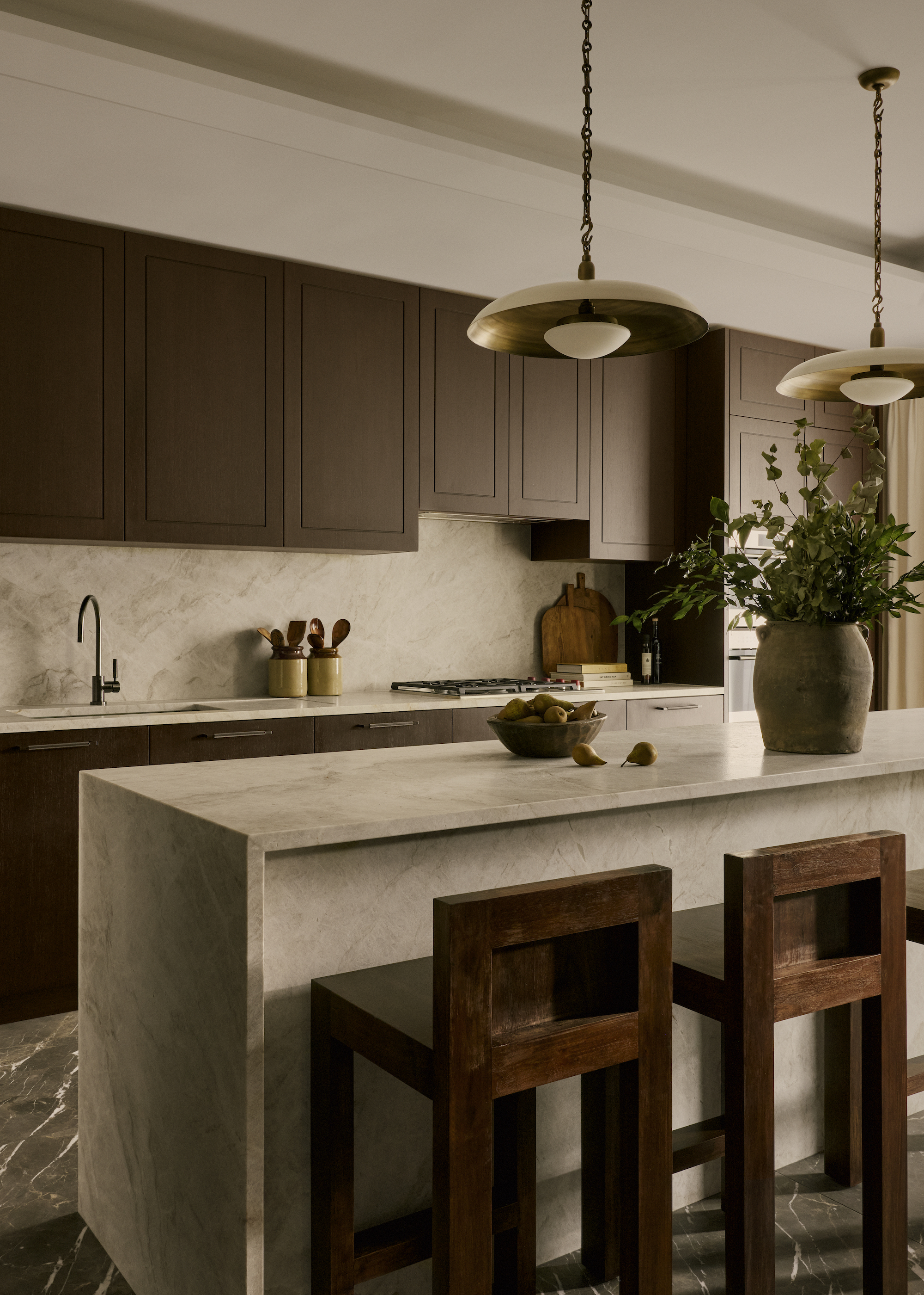 brown kitchen with marble island and wooden stools, with modern pendant lighting