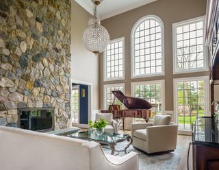 living room with stone feature wall large full length leaded windows grand piano and round chandelier