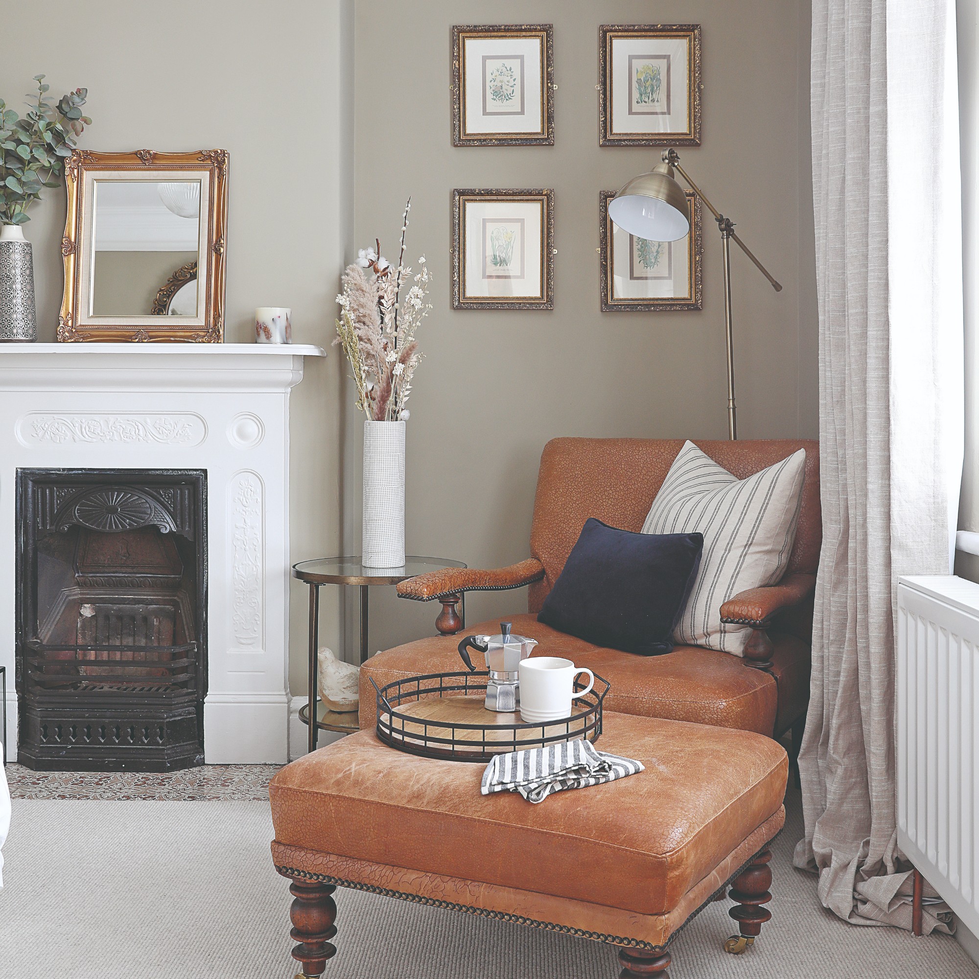 A neutral-painted living room with a brown leather chair and matching ottoman and a brass floor lamp in the corner