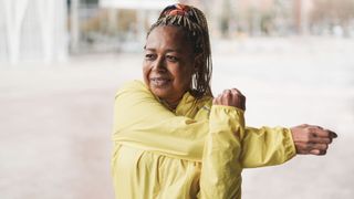 Woman smiling wearing bright yellow raincoat stretching outdoors