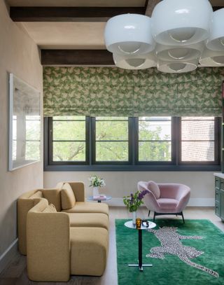 Living room with beige walls, pale yellow sofa, green rug and blinds and lilac armchair