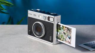 A print ejecting from a black and gray Fujifilm Instax mini Evo instant camera