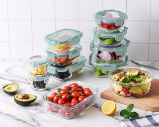 an assortment of glass food storage containers on a marble countertop with salad ingredients meal prepped in each