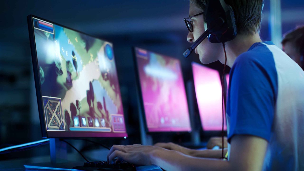 A man playing video games at a monitor in a row of several monitors.