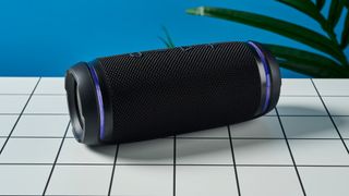 a black portable bluetooth speaker with LED panels sits atop a white table with a blue background