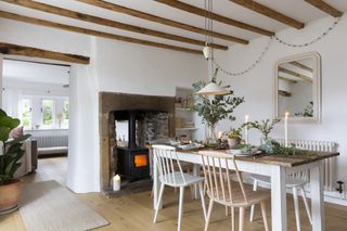 Slow living Scandi style Victorian cottage, with farmhouse table, spindle chairs, white walls and contrast wood beams, and lit stove.