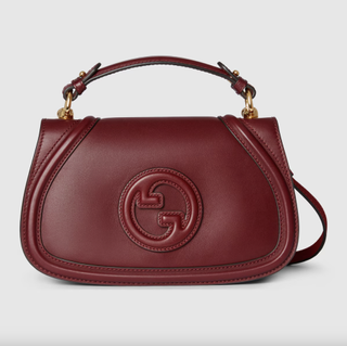 an oxblood gucci bag in front of a plain backdrop with a top handle