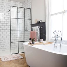 white bathroom with black framed shower screen, chrome shower head and Victorian radiator with freestanding bath tub and traditional mixer tap