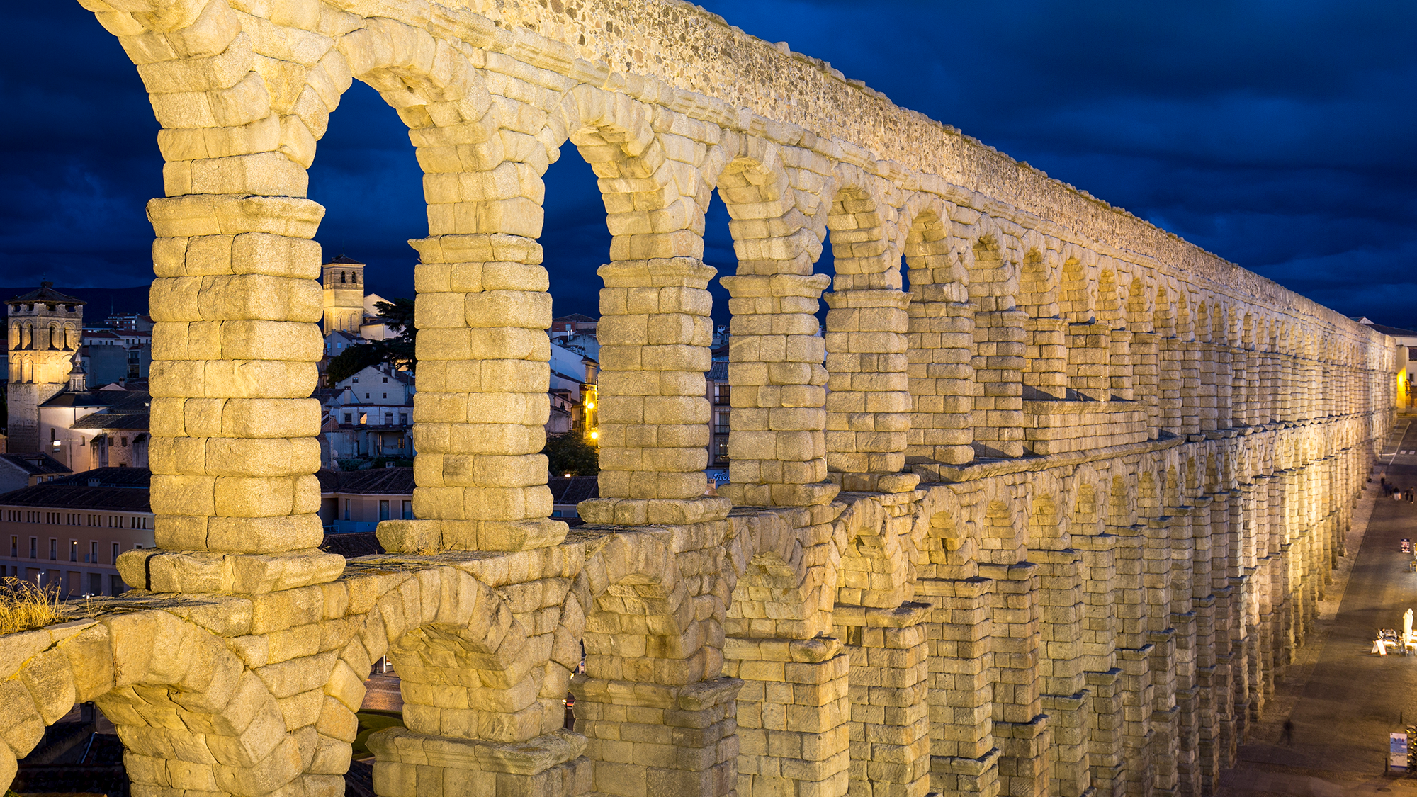 A view of a stone aqueduct in the middle of an ancient Italian city at night