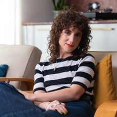 Pippa Toole poses for a portrait and wears a striped top whilst sitting on a sofa
