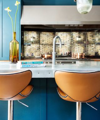 blue kitchen with large blue kitchen island, mirrored backsplash, orange bar stools, vase, large cooker hood