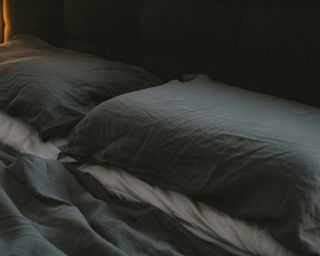 a close up shot of an empty bed and pillows lit by lamp light only