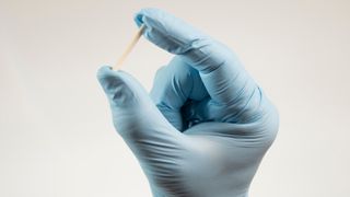 A gloved hand holds up a small rod-shaped implant