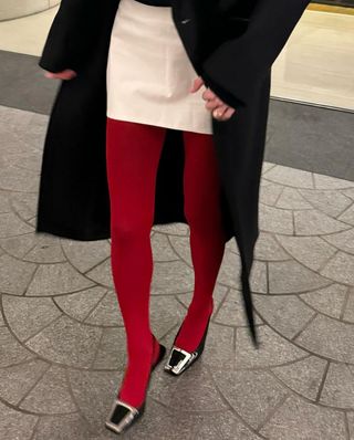 @helenannbyrne wearing red tights, cream skirt, black coat, and black heels