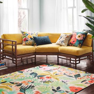 A floral rug sits in a multi-colored pattern sits next to a large L-shaped orange couch
