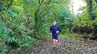 Running man in woods wearing Salomon Sense Flow wind jacket