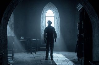 nicholas hoult's character, thomas, stands in a dark room. Just above his head is an arched window with a stream of white light coming through. There is shadow across his face so we can't really see his expression. He is looking ahead with the camera straight on.